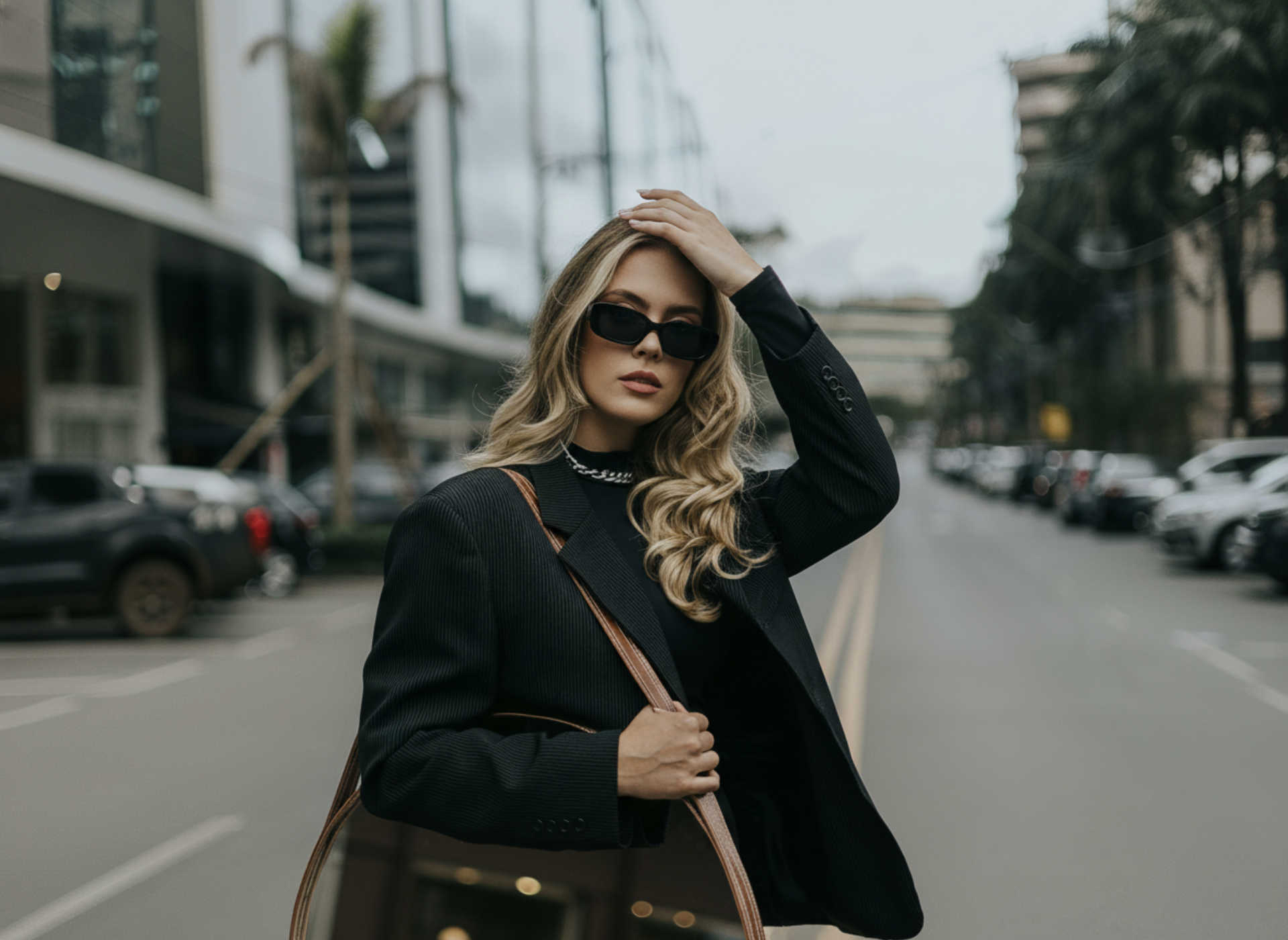 Woman in a black coat and sunglasses standing on a city street.
